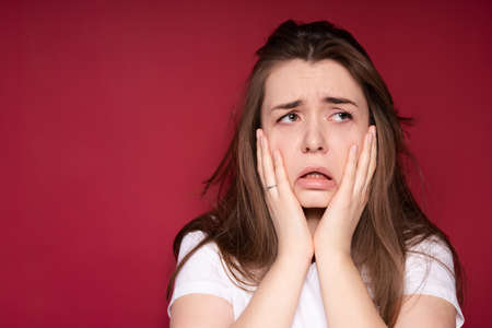 Sad young girl in a white T-shirt suffers from pain in the oral cavity touching her face with her...