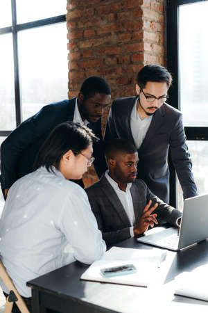 Group of Asian and African American workers in a meeting while standing near a table looking into a laptopの写真素材