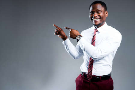 Happy african american businessman in shirt and tie points fingers to the side smiling. Place for...