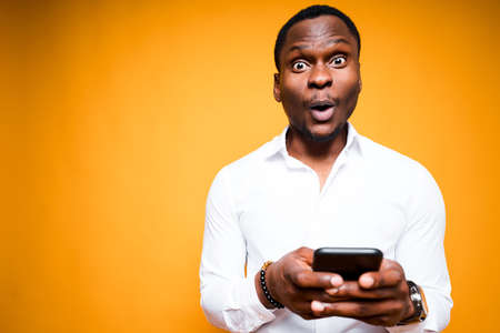 Handsome african american man holding a phone in his hand and is surprised by its power while...