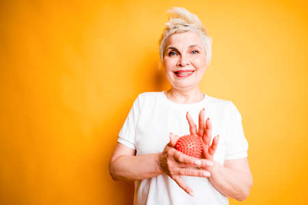 Cheerful adult woman in a white t-shirt smiles and massages a massage ball in her hands to relax...