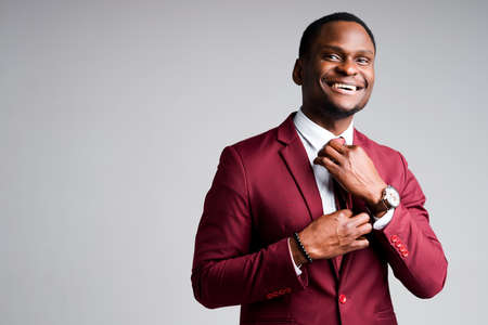 Smiling african american businessman straightens tie around neck and looking at cameraの写真素材