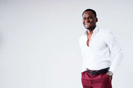 Cheerful dark-skinned man in a shirt and with one hand in his pants pocket looks at the camera and smilesの写真素材