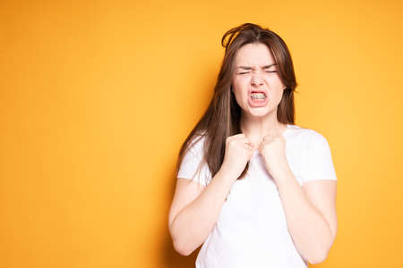 A girl with braces, closing her eyes in pain, clenches her hands into fists and pretends to hit herself in the jawの写真素材