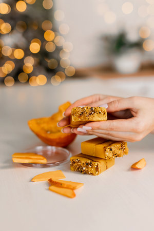 cropped shot of woman holding pumpkin slices on blurred christmas lights backgroundの写真素材