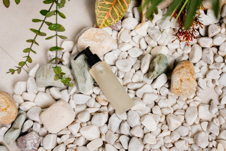 Cosmetic bottle on white pebbles background with green plant.