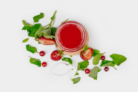 Jar of strawberry jam with fresh berries and green leaves on white background