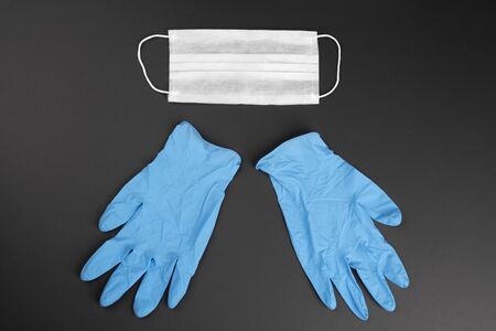 Corona virus pandemic concept: One white protection mask with ribbons and two blue gloves on mat...