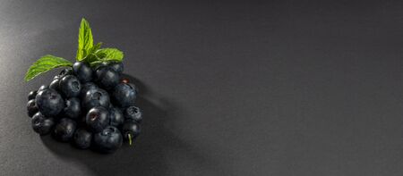 Amazing tasty natural and organic blueberry fruits stacked to a pyramid shape with some peppermint leaves. Light falls from behind on dark background with space for textの写真素材