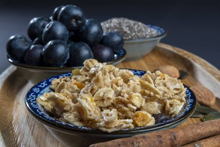 Healthy/natural food concept: On wooden board, some cinnamon sticks, almonds and sunflower seeds. Close up on crunchy granola, blueberries and chia seedsの写真素材