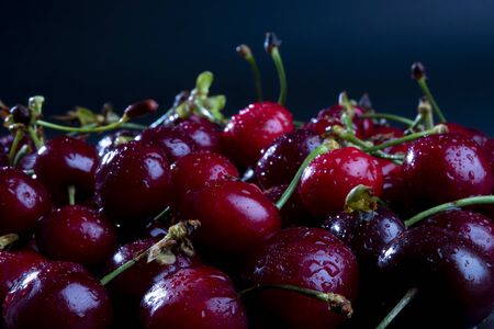Side view on stacked fresh, wet, dark cherries. Water drops on bright shiny dark red fruits with stalks. Dramatic black background with space for textの写真素材