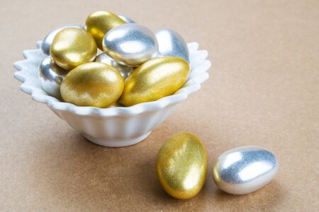 View from above on close up gold and silver glazed luxury almond candy treats in a white porcelain for special events. Sweet confections on brown background and copy spaceの写真素材