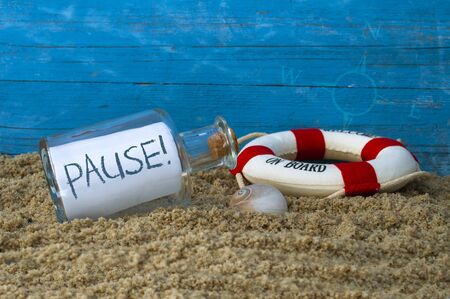 Message in a bottle with pause on sand with lifebuoy and blue weathered woodの写真素材