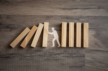 Wooden pieces with stick figure metaphor for stopping domino effect on wooden backgroundの写真素材