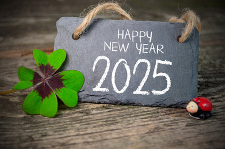 Wooden hang tag and slate with four leaf clover and sparklers with the German words for Happy New Year - Happy New Year 2025 on wooden weathered backgroundの写真素材