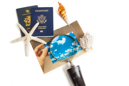 Picture On Isolated White Background of finger holding photo and a magnifying glass focus on the clouds in the blue sky with travel passport, starfish and sea shell ready for a peaceful, relaxing Getaway Vacationの写真素材