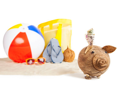 Coconut Piggy bank in foreground with Colorful Beach Ball, Star Fish and Sandals, Flip Flops in Beach Sand in background on isolated whiteの写真素材