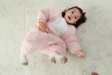 the sweet little girl was wearing a pink warm pajamas and smiling on the white carpetの写真素材