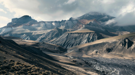 A towering mountain range dominates the scene, set against a backdrop of dramatic clouds in the sky. The jagged peaks of the mountains contrast with the soft, billowing clouds above.の素材