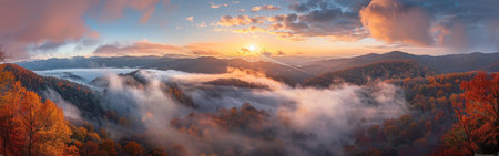 A panoramic view of a mountain range at sunset, with fog rolling through the forest below. The sky is filled with colorful clouds, and the sun is setting behind the mountains. The trees in the foreground are in autumn colors.の素材