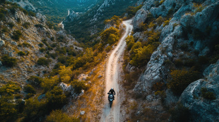 A rider navigates a winding dirt road through rocky mountains surrounded by lush greenery. The sunset casts a warm glow over the tranquil scene, creating a peaceful atmosphere.の素材