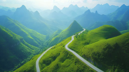 A winding road carves its way through verdant hills, surrounded by majestic mountains under a clear blue sky. This tranquil setting invites exploration and adventure.の素材