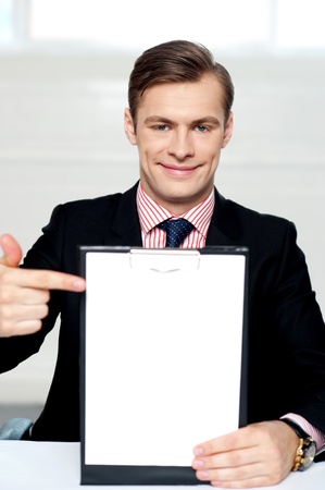 Smiling man pointing towards blank clipboard. Indoor shotの写真素材