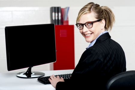 Business lady turning back and smiling at camera while typing on keyboardの写真素材