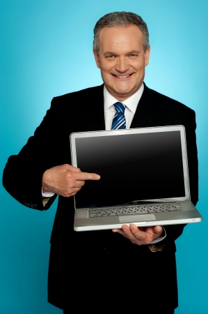 Aged corporate male pointing at laptop screen isolated over gradient backgroundの写真素材
