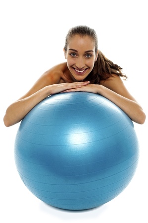 Woman leaning over big blue swiss ball and smiling at camera.の写真素材