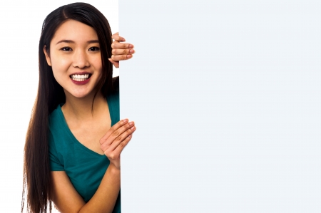 Smiling model popping from behind big blank whiteboardの写真素材