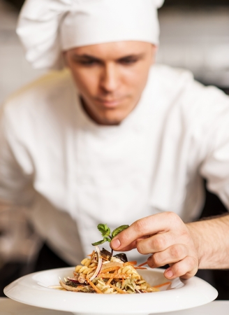 Handsome male chef dressed in white uniform decorating pasta saladの写真素材