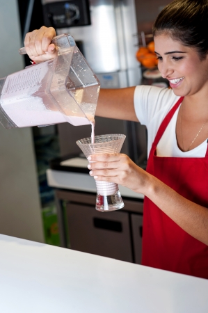 Attractive girl pouring strawberry shake in glassの写真素材
