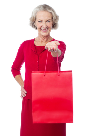 Smiling senior woman offering her red shopping bagの写真素材
