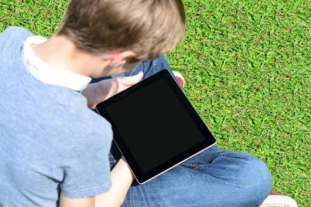 Boy sitting on lawn and using his new tablet pc