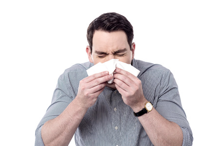 Sick man blowing his nose into a tissue, sneezing.