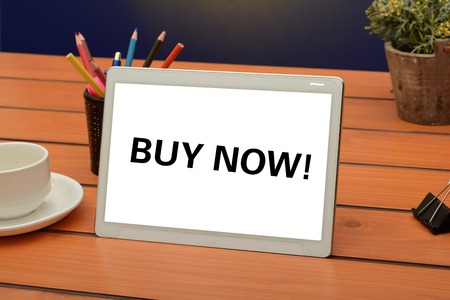 Buy now text on white tablet screen, sale concept on wooden backgroundの写真素材