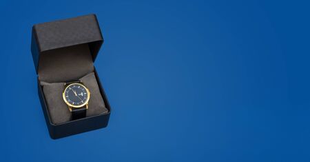 Luxury style golden hand watch in gift box on blue background with copy space.