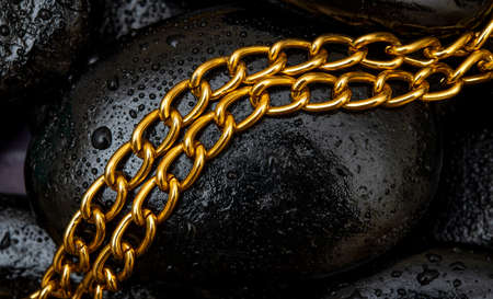 Golden color chain with wet black stones in background.の写真素材