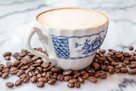 Coffee milk in a cup with coffee bean, rose patterned ceramic cup, on marble table in the morning light.の写真素材
