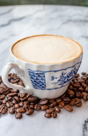 Coffee milk in a cup with coffee bean, rose patterned ceramic cup, on marble table in the morning light.の写真素材