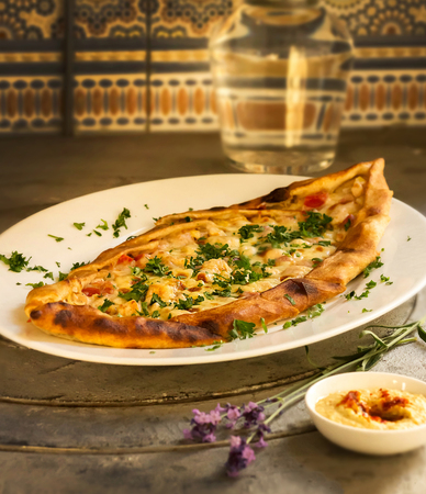 Pizza with chicken, cheese and greens lie on a plate. Next to the bowl with sauce and a branch of lavenderの写真素材