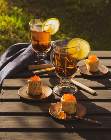Pancakes with red caviar, two glasses with tea and slices of lemons. Evening sunの写真素材