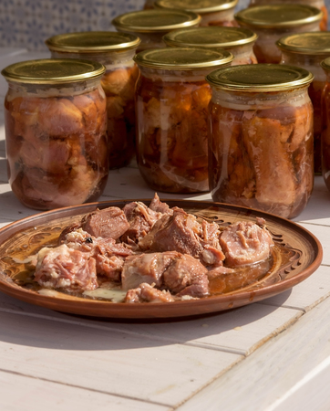 Canned meat in a glass jar on a white wooden table. Next plate with meatの写真素材