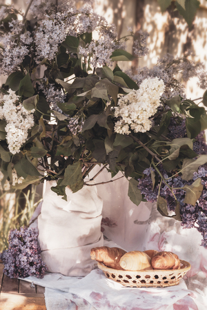 Croissants in a wicker basket on a background of lilac flowersの写真素材