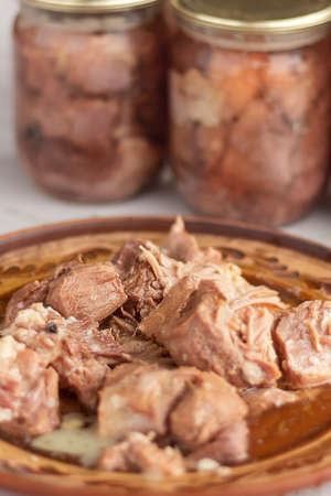 pieces of stew meat on a clay plate on the background of glass cans with home preservation. Home cookingの写真素材