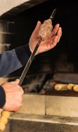 Man is stringing a Caucasian kebab on a skewer infront of cooking on a fireの写真素材