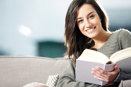 Portrait of a happy young woman lying on couch with bookの写真素材