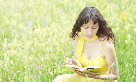 beautiful young woman reading book in a field full of yellow flowers