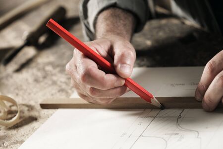 Closeup  view of a carpenter using a red pencil to draw a line on a blueprintの写真素材